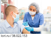 Doctor in a protective mask injects a vaccine to a man with syringe. Стоковое фото, фотограф Яков Филимонов / Фотобанк Лори