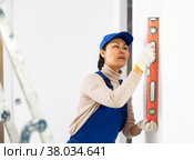 Woman in overalls checks the verticality of walls with a building level. Стоковое фото, фотограф Яков Филимонов / Фотобанк Лори