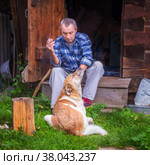 Russia Polevskoy August 2021: An elderly man relaxes near a Russian bathhouse with his dog and smokes a cigarette. Редакционное фото, фотограф Акиньшин Владимир / Фотобанк Лори