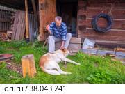 Russia Polevskoy August 2021: An elderly man relaxes near a Russian bathhouse with his dog and smokes a cigarette. Редакционное фото, фотограф Акиньшин Владимир / Фотобанк Лори