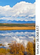 Calm autumn landscape with a mirror reflection of clouds in the blue water of a pond and mountain peaks in the distance. Siberia, Buryatia, Eastern Sayan Mountains, Tunka Valley. Стоковое фото, фотограф Виктория Катьянова / Фотобанк Лори