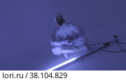 Man in chemical protection suite sitting in front of fluorescent lamp. Стоковое видео, видеограф Aleksey Kidisyuk / Фотобанк Лори