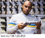 Latino choosing sporting and hunting revolvers in gunsmith shop. Стоковое фото, фотограф Яков Филимонов / Фотобанк Лори