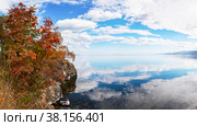 Autumn landscape of Baikal  Lake and Cape Shamansky. Red rowan bushes on rocky shore of Сape. Panoramic view of bay with reflection of clouds in calm water. Natural background. Autumn journey. Стоковое фото, фотограф Виктория Катьянова / Фотобанк Лори