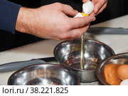 Chef breaks raw egg into bowl while preparing dough. Pastry chef cooks and breaks eggs. Process of breaking eggs for subsequent whipping and cooking. Concept culinary skills and catering. Copy space. Стоковое фото, фотограф Aleksandr Golubev / Фотобанк Лори