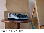 Old classic retro typewriter on dusty table in interior of room with art canvases in background against wall. View of Soviet-era typewriter. Copy space. Стоковое фото, фотограф Aleksandr Golubev / Фотобанк Лори