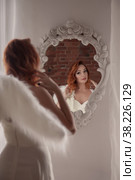 Pretty, slender woman with wings. Female in stage image of an angel. Emotions of girl in dress standing at mirror in an old textured interior room. Actress shows her abilities. Author space in photo. Стоковое фото, фотограф Aleksandr Golubev / Фотобанк Лори
