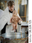 Infant baptism in Orthodox Church. Priest holds newborn child in his arms at baptismal font with Holy water. Baby is bathed in water. Sacrament rite of baptism. Редакционное фото, фотограф Aleksandr Golubev / Фотобанк Лори