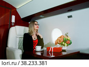 Cute young businesswoman with gift flying in luxury private jet. Business woman in airplane first class seat during trip. Concept quality of passenger service in aviation industry, travel at highest. Стоковое фото, фотограф Aleksandr Golubev / Фотобанк Лори