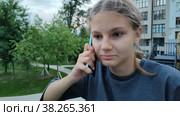 Красивая подросток девочка разговаривает по телефону в городском парке. Современные технологии и общение по смартфону. Мобильный телефон в руке симпатичной европейской девушки. Портрет ребенка, крупный план. Beautiful teen girl is talking on the phone in a city park. Modern technologies and communication via smartphone. Mobile phone in the hand of a pretty caucasian girl. Portrait of child, close-up. Стоковое видео, видеограф Ирина / Фотобанк Лори