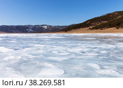 Baikal Lake in early spring on sunny day. Ice surface was covered with thawed patches and snow on ice became loose and wet. Coastal hills cleared of snow. Beautiful spring landscape. Natural background. Стоковое фото, фотограф Виктория Катьянова / Фотобанк Лори