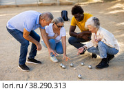 Positive mature diverse percioners comparing the distance of pumped balls after petangue at the sunny afternoon outdoors. Стоковое фото, фотограф Яков Филимонов / Фотобанк Лори