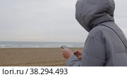 Woman in jacket surfing net on mobile near the sea on dull cold day. Стоковое видео, видеограф Данил Руденко / Фотобанк Лори