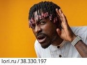 African young man in white shirt holding hand near ear on yellow background. Стоковое фото, фотограф Сергей Толмачёв / Фотобанк Лори