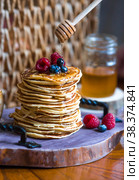 Delicious pancakes with honey, blueberries and raspberries. Next to it is a wooden barrel with an inscription in Russian: "honey". The concept of the Maslenitsa holiday. Стоковое фото, фотограф Photojuli / Фотобанк Лори