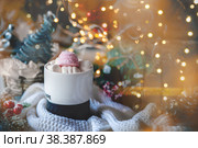 Cozy Christmas still life. The concept of warmth and comfort during the cold winter holidays. cup of coffee or hot chocolate with marshmallows on the Christmas table. glare of the garland adds a festive atmosphere. Стоковое фото, фотограф Оксана Медведева / Фотобанк Лори