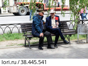RUSSIA, VOLGOGRAD - May 9, 2022: Two elderly men sit on a park bench during the day and hold a red flag. Volgograd. Редакционное фото, фотограф Владимир Арсентьев / Фотобанк Лори