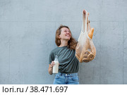 Современная стильная женщина со стеклянной бутылкой молока и авоськой купила хлеб. Девушка на фоне серой стены. Концепция здорового питания и экологии. Отказ от пластиковых пакетов. Стоковое фото, фотограф Photojuli / Фотобанк Лори