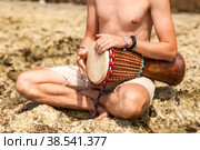 Close up young man drummer, playing rhythm with djembe drum, sitting at tropical coral reef coast background. Travel vacation and music relaxation concept. Selective focus. Copy text space. Стоковое фото, фотограф Aleksandr Golubev / Фотобанк Лори
