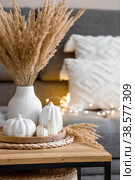 Still-life. Dried pampas grass in a vase, white ceramic pumpkins, a teapot, a cup and pumpkin-shaped candles on a coffee table in the home interior of the living room. Cozy autumn concept. Стоковое фото, фотограф Photojuli / Фотобанк Лори