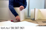 A man assembles a shelving unit. Connects panels with euro screws. Wooden modular rack. Assembling a modular rack. Стоковое видео, видеограф Vadzim Yakubovich / Фотобанк Лори