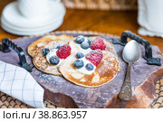 Delicious pancakes with honey, blueberries and raspberries. Next to it is a wooden barrel with an inscription in Russian: "honey". The concept of the Maslenitsa holiday. Стоковое фото, фотограф Photojuli / Фотобанк Лори