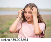 The girl squints. A teenage girl straightens her hair and covers her eyes from the bright light while standing in a spring meadow. Portrait of a sneezing girl. Стоковое фото, фотограф Александр Кротков / Фотобанк Лори