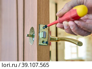Door latch plate is fastened with fixing screw, locksmith tightens fastener with screwdriver. Стоковое фото, фотограф Владимир Григорьев / Фотобанк Лори