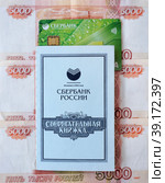 Сберегательная книжка Сбербанка России, пластиковая карта лежат на российских денежных купюрах (2023 год). Редакционное фото, фотограф Цибаев Алексей / Фотобанк Лори