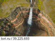 Aerial top down view of Hengifoss waterfall in East Iceland. The third highest waterfall in Iceland and is surrounded by basaltic strata with red layers of clay between the basaltic layers (2020 год). Стоковое фото, фотограф Igor Tichonow / Фотобанк Лори