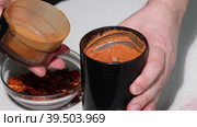 A man grinds dried red peppers in a coffee grinder. Demonstrates the degree of grinding in a coffee grinder. Grinding hot pepper. Close-up. Стоковое видео, видеограф Vadzim Yakubovich / Фотобанк Лори
