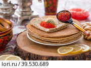 Русские традиции. Русский праздник Масленица. Натюрморт с чашкой чая, стопкой блинов, красной икрой, лимоном, рогаликами, леденцовым петушком, деревянными ложками (хохлома) и самоварами. Стоковое фото, фотограф Photojuli / Фотобанк Лори