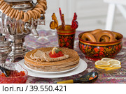 Русские традиции. Русский праздник Масленица. Натюрморт с чашкой чая, стопкой блинов, красной икрой, лимоном, рогаликами, леденцовым петушком, деревянными ложками (хохлома) и самоварами. Стоковое фото, фотограф Photojuli / Фотобанк Лори