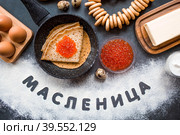 Русские традиции. Русский праздник Масленица. Стопка блинчиков, красная икра, бублики, рогалики, деревянная ложка, яйца и сливочное масло. Надпись на русском языке "Масленица" написано мукой. Вид сверху. Стоковое фото, фотограф Photojuli / Фотобанк Лори