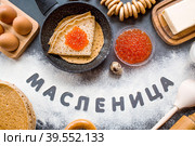 Русские традиции. Русский праздник Масленица. Стопка блинчиков, красная икра, бублики, рогалики, деревянная ложка, яйца и сливочное масло. Надпись на русском языке "Масленица" написано мукой. Вид сверху. Стоковое фото, фотограф Photojuli / Фотобанк Лори