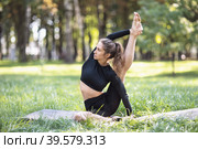 Young woman in black sportswear practicing yoga doing surya yantrasana exercise, compass pose, exercising on a summer morning in the park sitting on a mat. Стоковое фото, фотограф Сергей Чайко / Фотобанк Лори