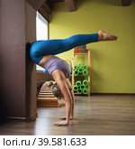 A woman practicing yoga, performs a handstand, inverted asana, trains in a fitness center in sportswear, leaning her booty against the wall. Стоковое фото, фотограф Сергей Чайко / Фотобанк Лори