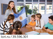 Female teacher, conducting extracurricular lesson in the school class tells schoolchildren the history of Argentina and shows national flag of country. Стоковое фото, фотограф Яков Филимонов / Фотобанк Лори