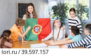 Female teacher, conducting extracurricular lesson in the school class tells schoolchildren the history of Portugal and shows national flag of country. Стоковое фото, фотограф Яков Филимонов / Фотобанк Лори