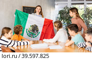 Female teacher, conducting extracurricular lesson in the school class tells schoolchildren the history of Mexico and shows national flag of country. Стоковое фото, фотограф Яков Филимонов / Фотобанк Лори