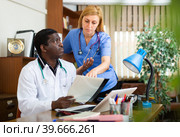Two focused doctors discussing medical histories of patients. Стоковое фото, фотограф Яков Филимонов / Фотобанк Лори