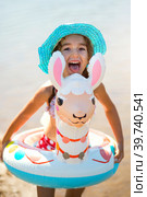 Girl in a hat it stands on the shore with inflatable circle in the shape of a lama. Inflatable alpaca for a child. Sea with a sandy bottom. Beach holidays, swimming, tanning, sunscreens. Стоковое фото, фотограф Ольга Симонова / Фотобанк Лори