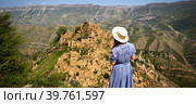 Female tourist high in mountains of Dagestan admires the breathtaking panoramic view of nature and the ancient abandoned city of Gamsutl. Caucasus mountains, tourist attraction, ruins, trekking tour. Стоковое фото, фотограф Ольга Симонова / Фотобанк Лори