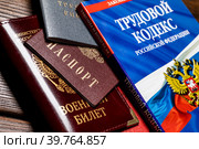 Паспорт, военный билет, трудовая книжка сотрудника и Трудовой кодекс Российской Федерации лежат на столе в отделе кадров предприятия (2023 год). Редакционное фото, фотограф Николай Винокуров / Фотобанк Лори