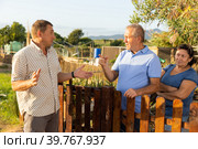 Quarrel of neighbors in country in village. Elderly couple and neighbor are in conflict near wooden fence. Стоковое фото, фотограф Яков Филимонов / Фотобанк Лори