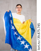 Joyous young woman holding Bosnia flag against unicoloured background. Стоковое фото, фотограф Яков Филимонов / Фотобанк Лори