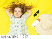 Girl posing for a travel agency on a yellow background, sunglasses, straw hat and sunscreen lie near her. Top view. Summer concept. Стоковое фото, фотограф Ирина Михайличенко / Фотобанк Лори