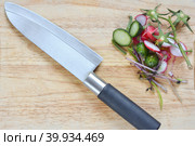 Vegetable peeling on a  light wood cutting board with big knife. After cooking vegetable salad: the remains of radish, cucumber, tomato, greens. Overhead view. Овощные очистки и нож лежат на оске после приготовление салата. Стоковое фото, фотограф Тамара Сахарова / Фотобанк Лори