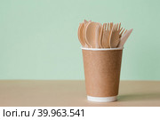 Экологически чистая одноразовая кухонная утварь в бумажном стаканчике на бежево-зеленом фоне. Деревянные вилки, ложки и ножи. Экология, концепция нулевых отходов. Стоковое фото, фотограф Photojuli / Фотобанк Лори