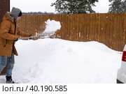 A man in winter cleans snow with a shovel in the yard of a house in the parking lot. Snowfall, difficult weather conditions, the car is stalling, digging up the passage. Стоковое фото, фотограф Ольга Симонова / Фотобанк Лори